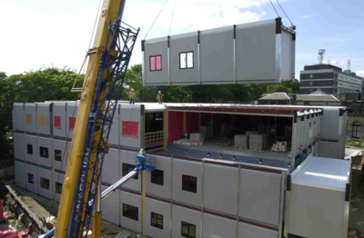 An image of a modular building being being assembled together by a crane.